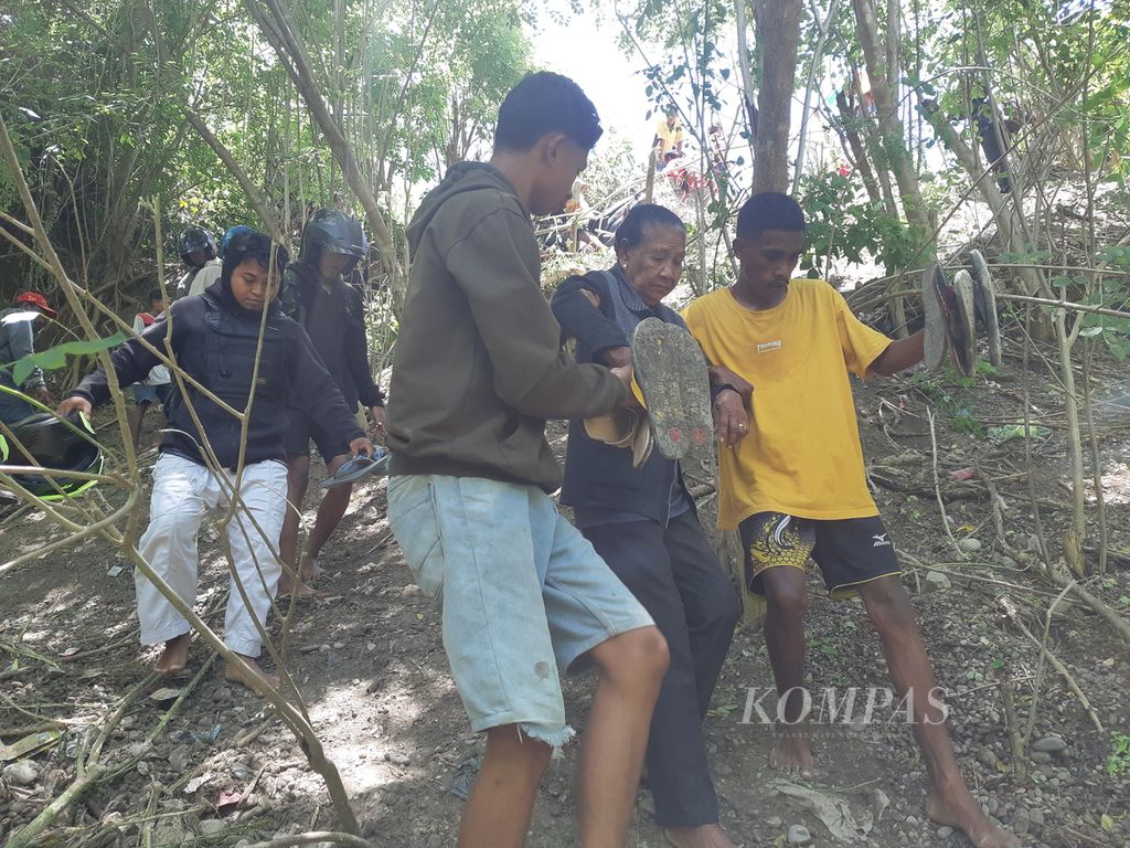 Seorang nenek dipapah saat menuruni jalan setapak yang terjal lantaran terjadi longsor di ruas Jalan Timor Raya, tepatnya Kelurahan Takari, Kabupaten Kupang, Nusa Tenggara Timur pada Minggu (19/2/2022). Longsor itu menyebabkan akses utama di Pulau Timor lumpuh total.