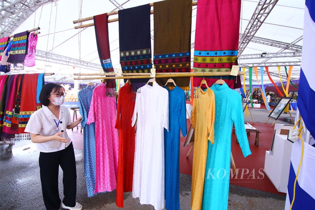 Seorang sukarelawan menunjukkan <i>ao dai</i>, baju tradisional wanita Vietnam, yang dipamerkan dan dijual di Hanoi Great Souvenirs 2022 di seberang Stadion My Dinh, Hanoi Vietnam, Jumat (13/5/2021). Kendati terasa kurang semarak dengan ornamen dan pernak-pernik SEA Games, warga merasakan SEA Games membawa dampak positif bagi perekonomian.