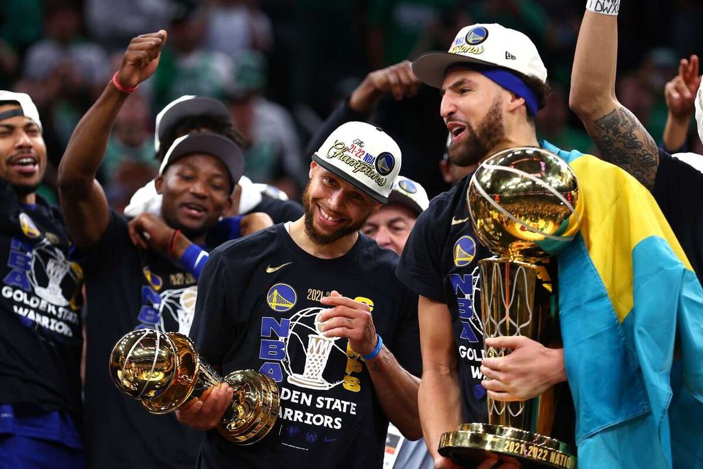Pemain Golden State Warriors, Klay Thompson (kanan), memegang piala juara NBA dan Stephen Curry memegang piala Most Valuable Player (MVP) setelah tim mereka memenangi gim keenam final NBA 2022 di TD Garden, Boston, AS, Jumat (17/6/2022). Warriors menang dengan skor 103-90 dan membuat kedudukan menjadi 4-2.