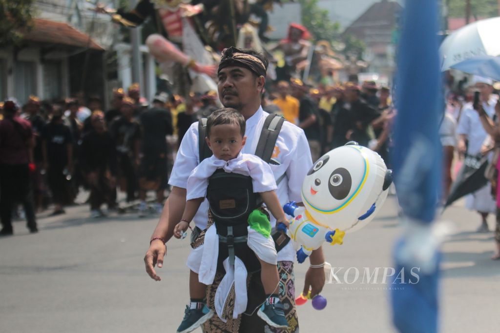 Tampak seorang balita digendong oleh ayahnya menjadi salah seorang peserta pawai.