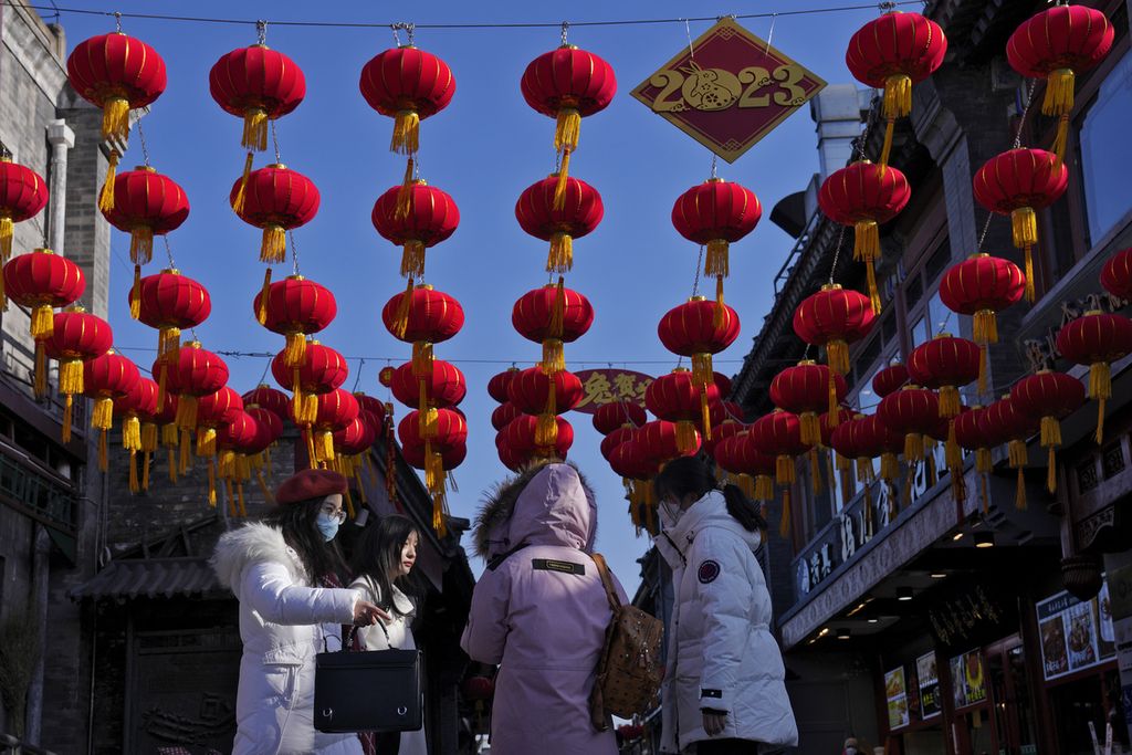 Para wanita berjalan di bawah lampion merah yang digantung di gang pusat perbelanjaan dekat Danau Houhai untuk merayakan Imlek di Beijing, China, Senin (16/1/2023). WHO mengimbau China untuk terus merilis informasi tentang gelombang Covid-19 di negaranya setelah pemerintah mengumumkan hampir 60.000 kematian sejak awal Desember lalu.