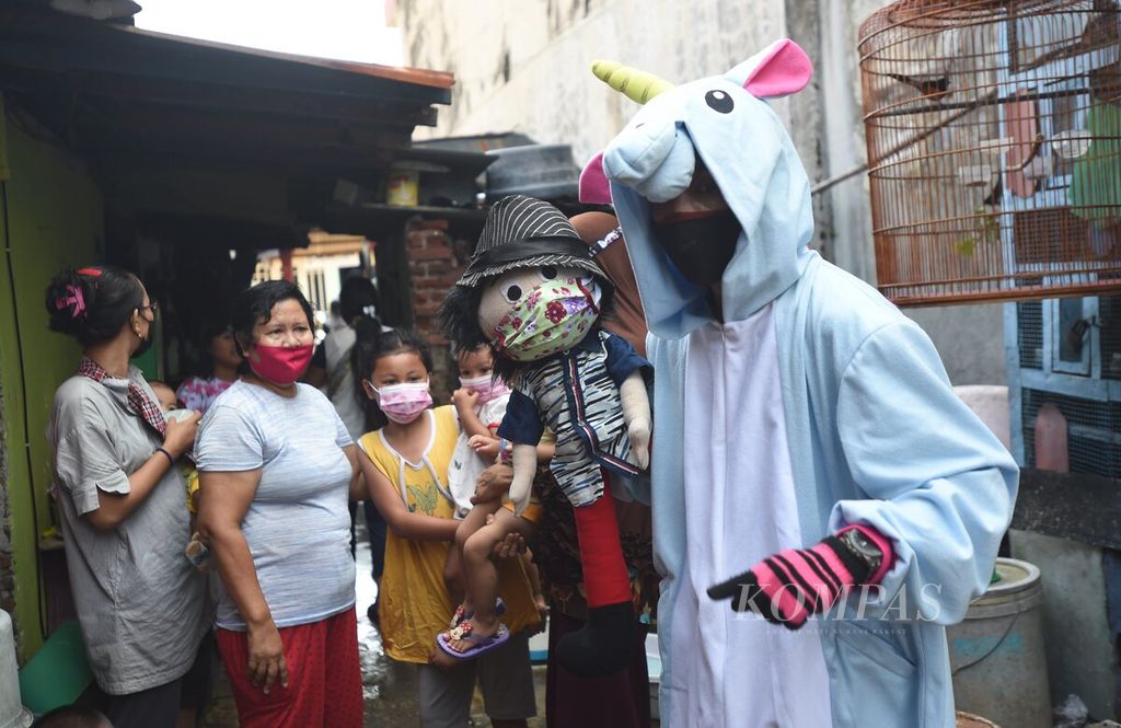 Pendongeng Harris Rizki Akhiruddin dengan membawa boneka tangan dan menggunakan kostum unicorn menyapa warga di kampung padat penduduk di kawasan Plemahan Kelurahan Kedungdoro, Kecamatan Tegalsari, Surabaya, Jawa Timur, Jumat (19/3/2021). Selain untuk menyambut World Puppetry Day, kegiatan mendongeng di permukiman tersebut merupakan kampanye sadar protokol kesehatan. 
