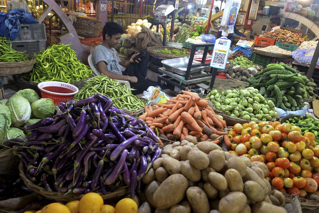 A vendor uses his mobile phone while waiting for the customers at a wholesale vegetable market in Hyderabad on May 19, 2022.