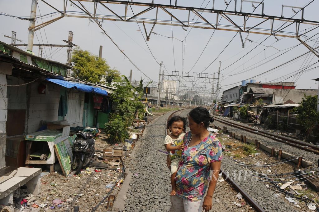 Warga mencari udara segar di ruang terbuka yang berada di antara jalur kereta yang membelah hunian semipermanen padat penduduk di kawasan Pademangan, Jakarta Utara, Kamis (17/7/2023).