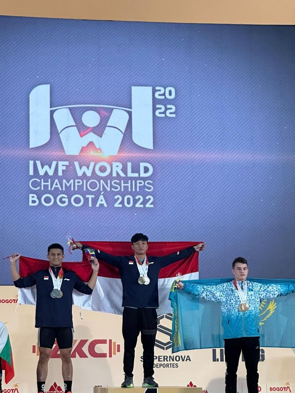 Lifter muda Indonesia Rahmat Erwin Abdullah (tengah) meraih emas kelas 73 kilogram dan memecahkan rekor dunia angkatan <i>clean & jerk</i> dengan 200 kg dalam Kejuaraan Dunia Angkat Besi 2022 di Gran Carpa Americas Corferias, Bogota, Kolombia, Sabtu (10/12) waktu Indonesia. Kesuksesan Rahmat disempurnakan oleh rekannya di pemusatan latihan nasional, Rizki Juniansyah (kiri), yang merebut perak kelas tersebut. 