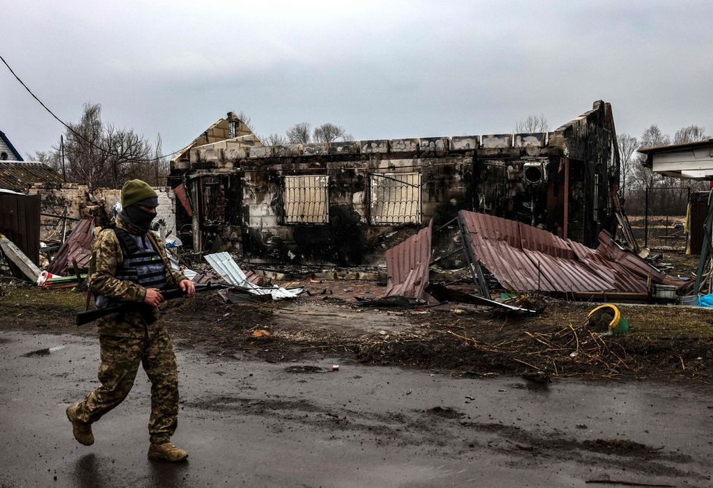 Seorang tentara Ukraina berpatroli di dekat rumah yang terbakar di Desa Lukianivka, dekat Kiev, Rabu (30/3/2022).