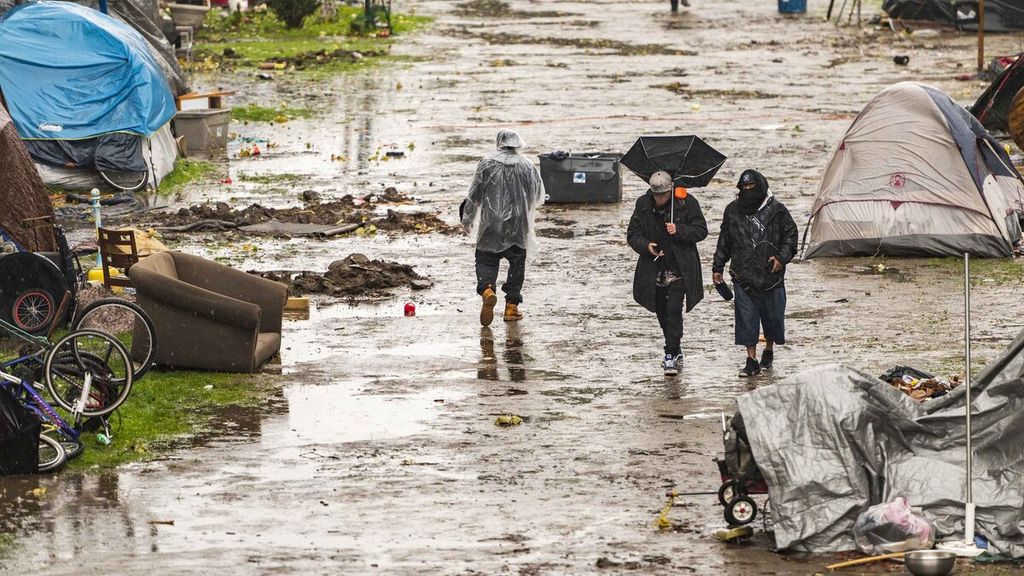 Warga melintas di area perkemahan tunawisma yang diterjang luapan Sungai San Lorenzo di Santa Cruz, California, Amerika Serikat, Senin (13/12/2021). Sebuah badai besar yang mendera wilayah California Utara yang disertai hujan dan salju diduga akan membesar hingga menyebabkan gangguan perjalanan serta kemungkinan terjadi banjir. Cuaca ekstrem seperti ini terjadi setelah musim gugur yang panas dan kering di belahan AS barat.