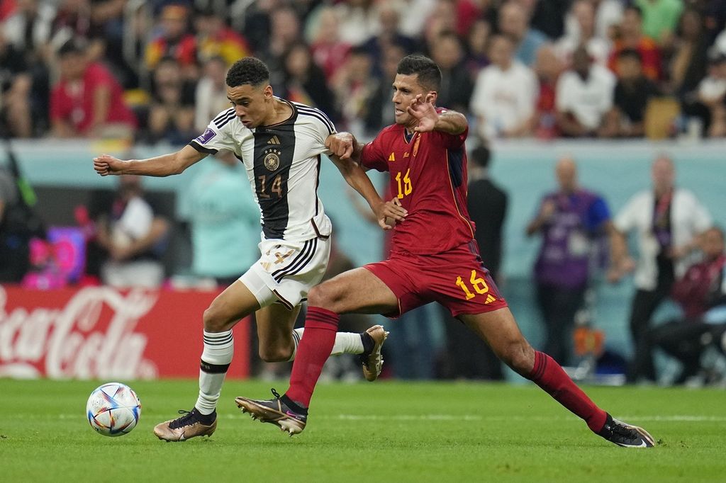 Gelandang serang Jerman, Jamal Musiala (kiri), berebut bola dengan gelandang Spanyol, Rodri, pada laga penyisihan Grup E Piala Dunia Qatar 2022 di Stadion Al Bayt Stadium, Al Khor, Qatar, Minggu (27/11/2022). Laga itu berakhir imbang 1-1. 