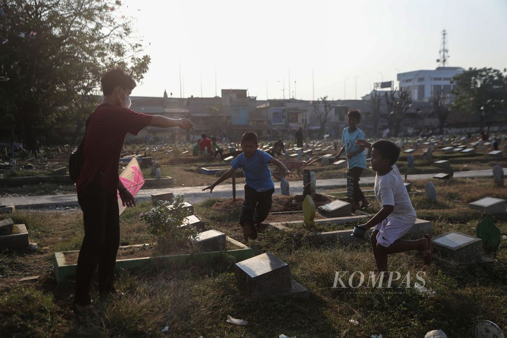 Tiga anak saling berebut layangan yang diberikan seorang remaja di Tempat Pemakaman Umum (TPU) Prumpung, Jatinegara, Jakarta Timur, Kamis (24/8/2023). 