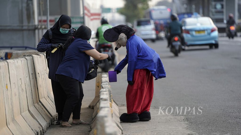 Pejalan kaki memberikan uang kepada badut Mickey Mouse yang berjalan gontai di Jalan MT Haryono, Jakarta Timur, Rabu (8/7/2020).