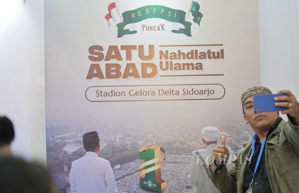 Seorang nahdliyin berswafoto dengan latar poster Resepsi Puncak Satu Abad Nahdlatul Ulama di Kantor Pusat PBNU, Jakarta, saat digelar konferensi pers menjelang acara tersebut, Jumat (27/1/2023). Kemajuan teknologi memunculkan pertanyaan terkait dengan hubungan antara manusia dan teknologi.