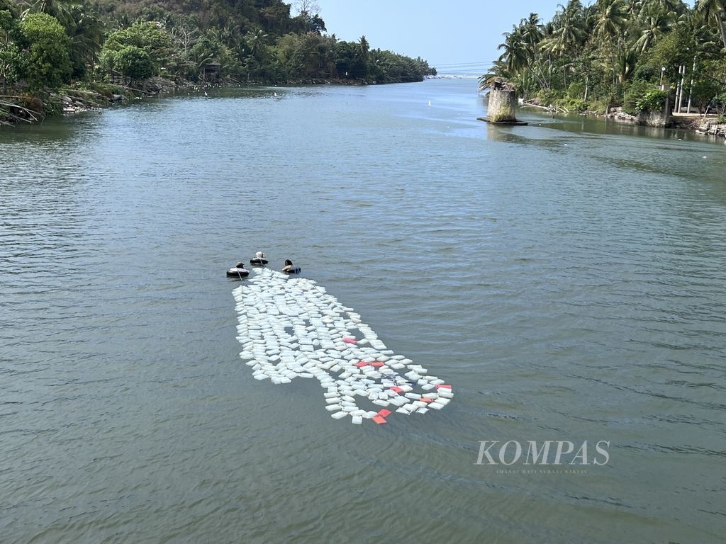 <i>Passau’ wai </i>berenang di Sungai Mandar, Polewali Mandar, Sulawesi Barat, Jumat (15/9/2023), dengan membawa rangkaian jeriken berisi air bersih. Air ini akan dijual untuk keperluan air bersih.