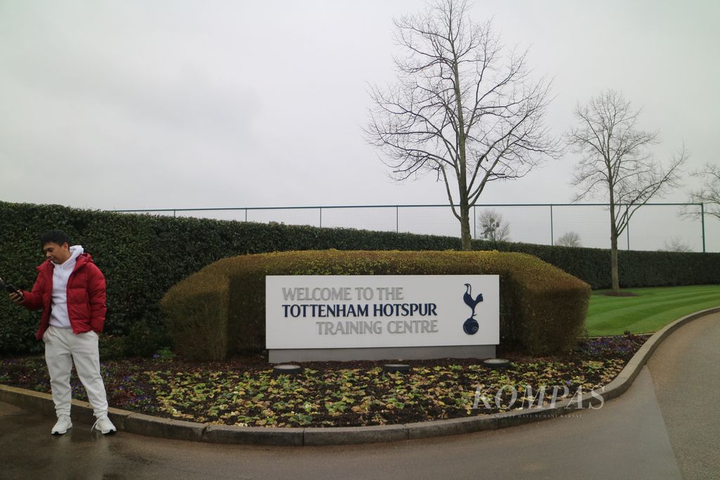 Seorang pengunjung berpose di depan gerbang masuk Tottenham Hotspur Training Centre, Enfield, London, Sabtu (25/2/2023). Pusat latihan bagi skuad Spurs itu dibangun seluas 31 hektare dan dilengkapi berbagai fasilitas canggih, seperti kolam renang, kompleks hidroterapi, ruang gimnasium berskala besar, serta 15 lapangan rumput.