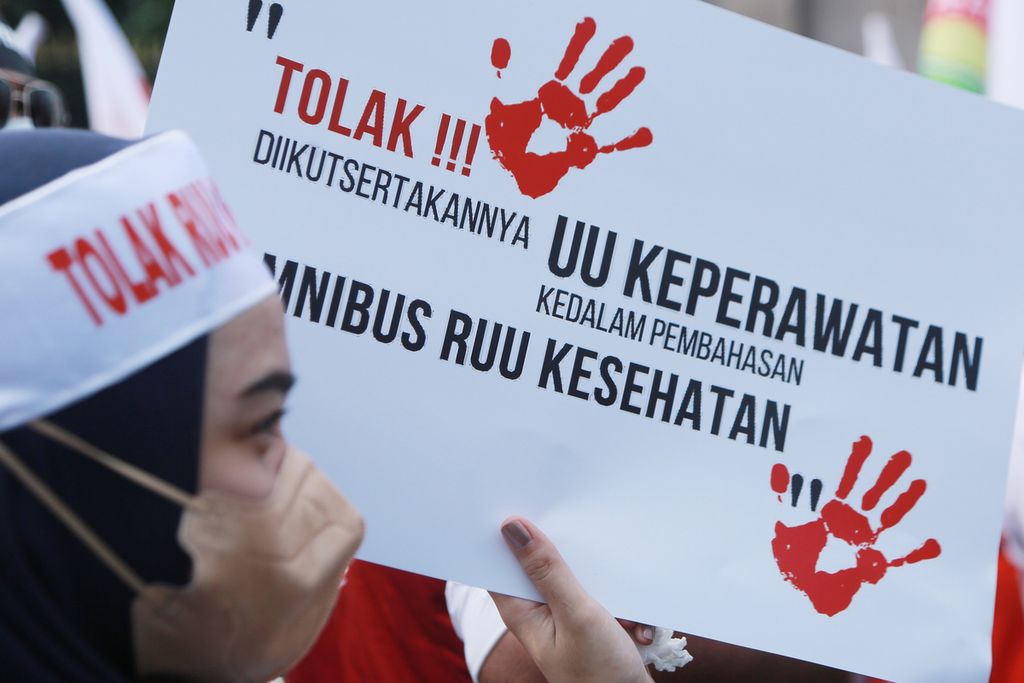 Tenaga kesehatan membawa poster saat demo tolak RUU Kesehatan Omnibus Law di depan Gedung DPR, Jakarta, Senin (28/11/2022). Demo digelar untuk mendesak anggota DPR mencabut RUU Kesehatan Omnibus Law dari Program Legislasi Nasional (Prolegnas) prioritas pada tahun 2023. Selain itu, massa aksi juga menuntut menolak adanya kapitalisasi kesehatan karena dianggap mengorbankan hak kesehatan rakyat. Massa aksi juga menolak pelemahan profesi dan penghilangan peran organisasi profesi melalui RUU Kesehatan Omnibus Law. 