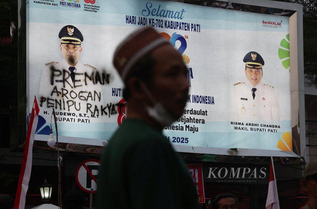 Warga dengan latar belakang papan iklan wajah Bupati Pati Sudewo dengan tulisan nada kecaman saat berlangsungnya penolakan kenaikan Pajak Bumi dan Bangunan Perdesaan dan Perkotaan (PBB-P2) hingga 250 persen di depan Kantor Bupati Pati, Kabupaten Pati, Jawa Tengah, Selasa (12/8/2025). 