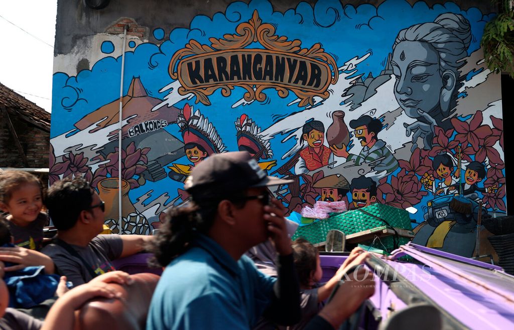 Mobil wisata melintasi salah satu akses jalan dengan latar belakang mural yang menghiasi tembok rumah warga di Desa Klipoh, Kecamatan Borobudur, Kabupaten Magelang, Jawa Tengah, Minggu (7/7/2024). Desa sentra kerajinan gerabah tersebut tidak hanya memproduksi perkakas alat rumah tangga dari tanah liat, tetapi berkembang sebagai tujuan desa wisata. 