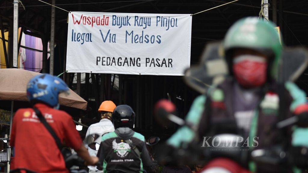 Spanduk ajakan untuk mewaspadai praktik pinjaman <i>online</i> ilegal menghiasi pintu masuk Pasar Muara Angke, Penjaringan, Jakarta Utara, Minggu (14/11/2021). Saat ini setidaknya telah ada lebih dari 19.700 pengaduan soal pinjaman daring ilegal ke Otoritas Jasa Keuangan. Bukan hanya soal bunga tinggi yang tidak disadari oleh nasabah, praktik penagihan utang juga sering kali menerapkan intimidasi.