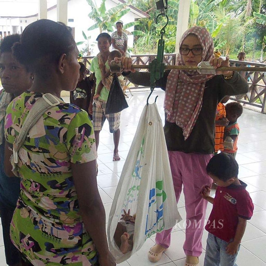 Dokter Rini Rahman (kanan) menimbang berat bayi di Balai Desa Kibay, Kecamatan Arso Timur, Kabupaten Keerom, Papua, pertengahan Agustus 2015. Rini dokter PTT yang bertugas di daerah pedalaman di Keerom. Ia turut membawa anaknya, Badranaya (baju merah).