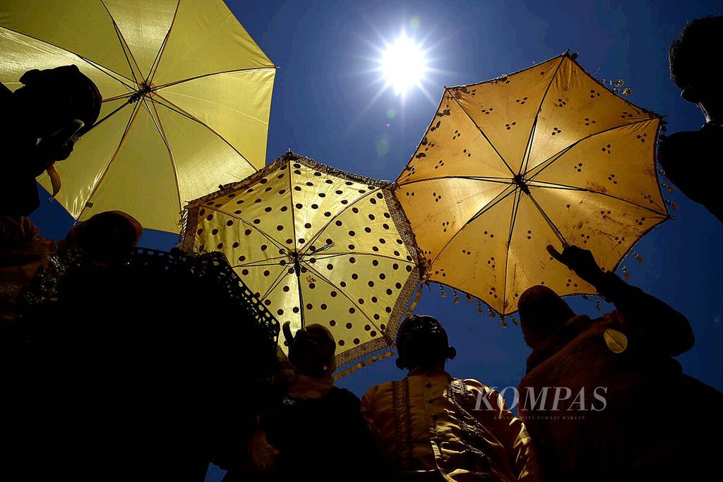 Warga mengenakan payung untuk mengindari terik matahari saat hadir dalam pembukaan Festival Gerhana Matahari Total di Desa Pakuli Utara, Kabupaten Sigi, Sulawesi Tengah, Minggu (6/3). Beragam aktivitas seni budaya diselenggarakan untuk menyambut gerhana matahari total, Rabu 9 Maret mendatang.