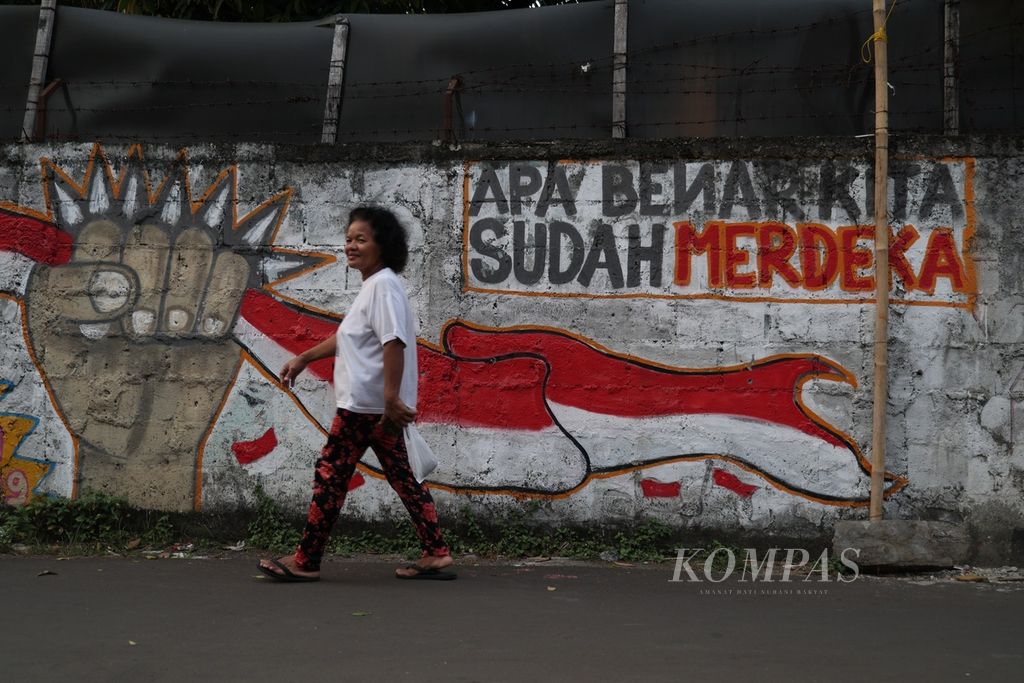 Warga melintas di dekat mural yang bertema menyambut kemerdekaan di Kampung Poncol, Tangerang Selatan, Banten, Minggu (11/8/2024).  