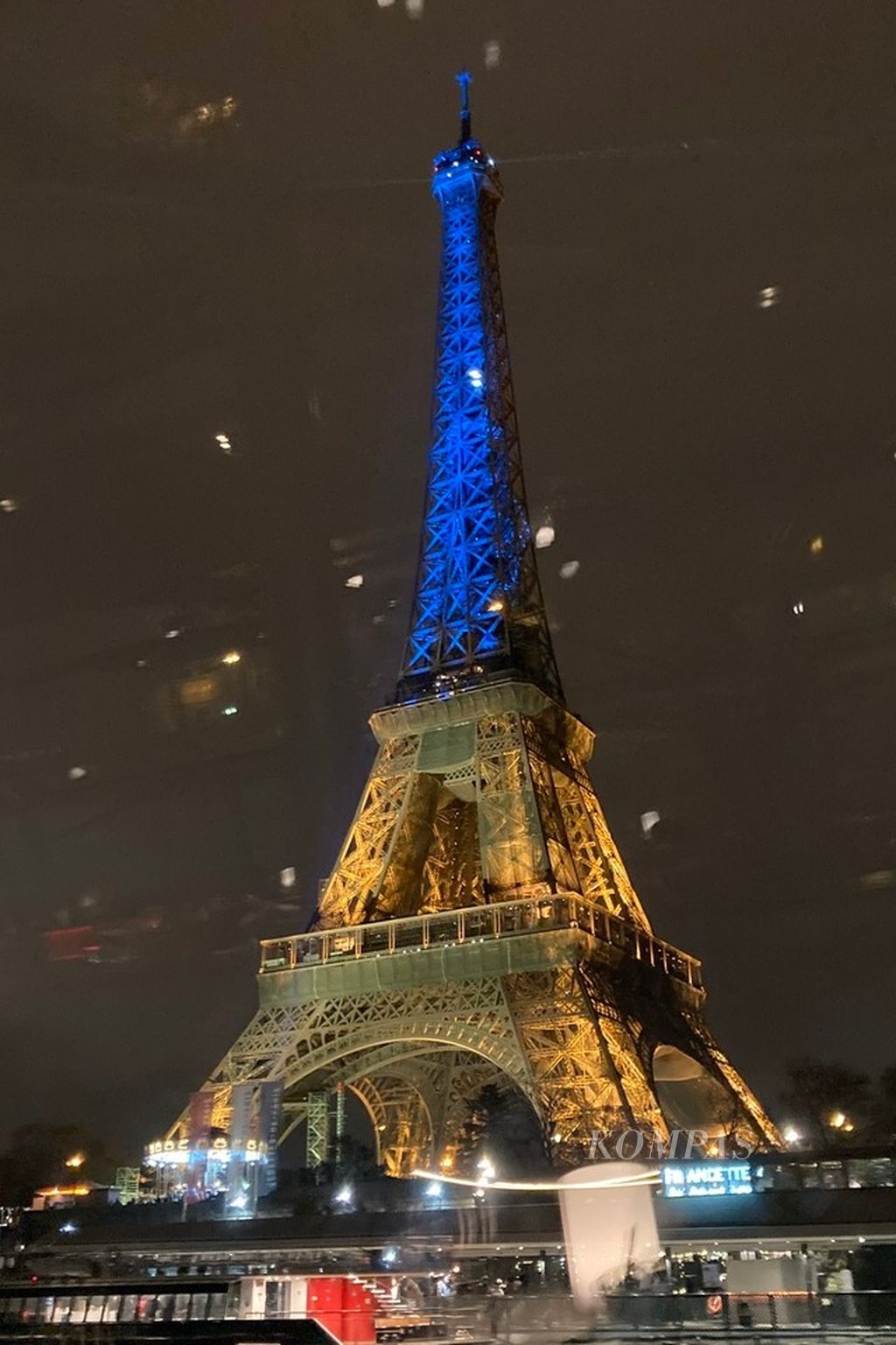 Menara Eiffel disorot lampu dengan warna bendera Ukraina untuk memperingati satu tahun invasi Rusia atas negara itu pada Kamis (23/2/2023) malam. Foto diambil dari balik kaca jendela Bateau Parisien, perahu wisata yang melintasi Sungai Seine di tengah kota Paris, Perancis. 