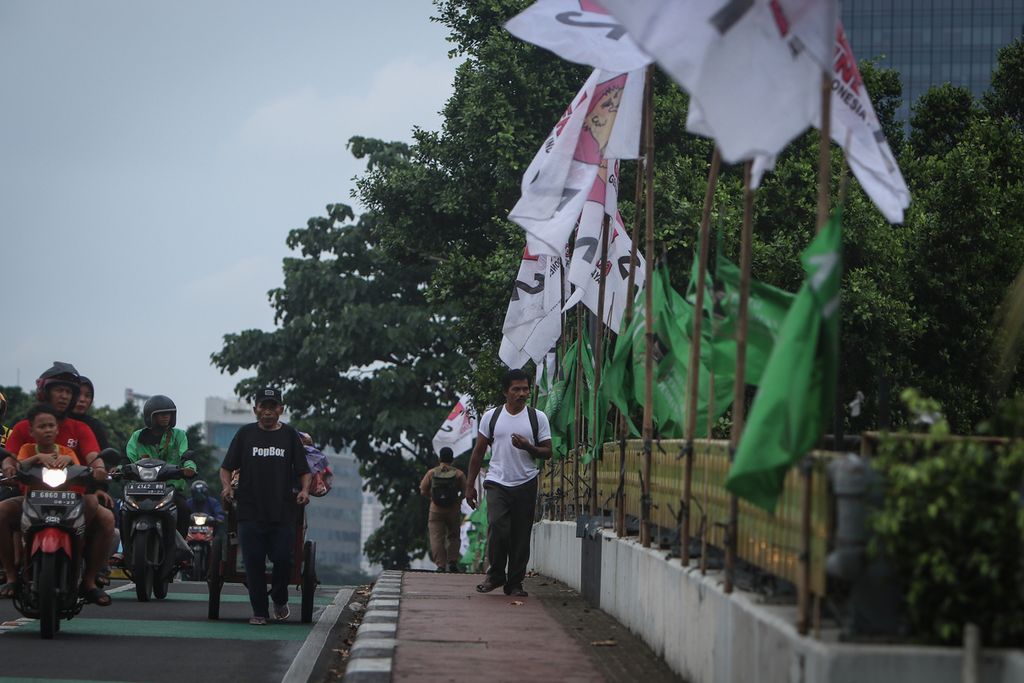 Warga melintas di samping bendera partai politik yang terpasang pada pembatas jembatan di Jalan Gatot Subroto, Jakarta, Selasa (7/2/2023). Sejumlah partai politik mulai memasang bendera dan spanduk untuk menarik perhatian calon pemilih. Sebelumnya, KPU telah menetapkan 18 partai sebagai peserta Pemilu 2024.