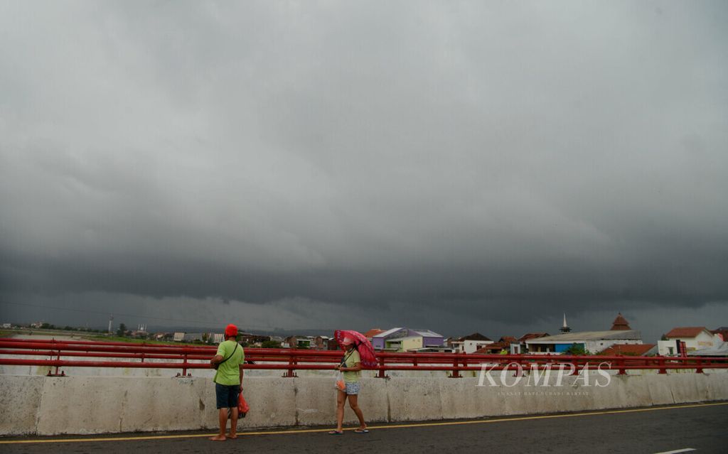 Warga berjalan di atas jembatan Banjir Kanal Timur dengan latar belakang cuaca mendung di Kota Semarang, Jawa Tengah, Minggu (7/2/2021). Dalam beberapa hari ini, cuaca ekstrem dengan curah hujan tinggi terjadi di sejumlah wilayah Jawa Tengah hingga berpotensi bencana.