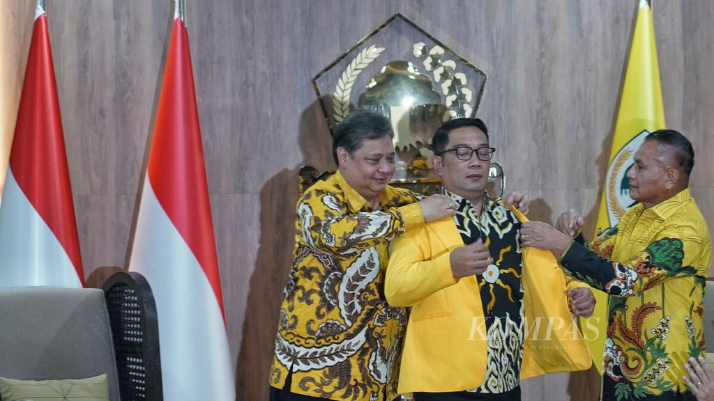 Ketua Umum Partai Golkar Airlangga Hartarto (kiri) dibantu Sekretaris Jenderal Partai Golkar Lodewijk Freidrich Paulus (kanan) memakaikan jas partai kepada Gubernur Jawa Barat Ridwan Kamil (tengah) di Kantor DPP Partai Golkar, Slipi, Jakarta, Rabu (18/1/2023). 