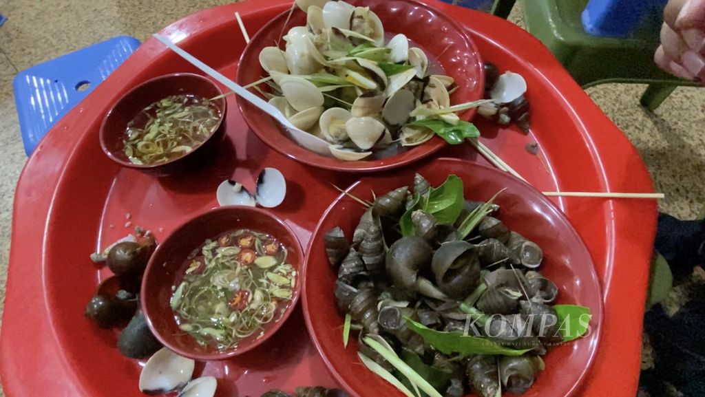 Ngao atau kerang Vietnam (atas) dan oc van atau siput yang dijual di kawasan Old Quarter, Hanoi, Vietnam, Sabtu (14/5/2022). Warga harus mencungkil kerang lalu mencelupkannya ke kuah bumbu (kiri) untuk memakannya.