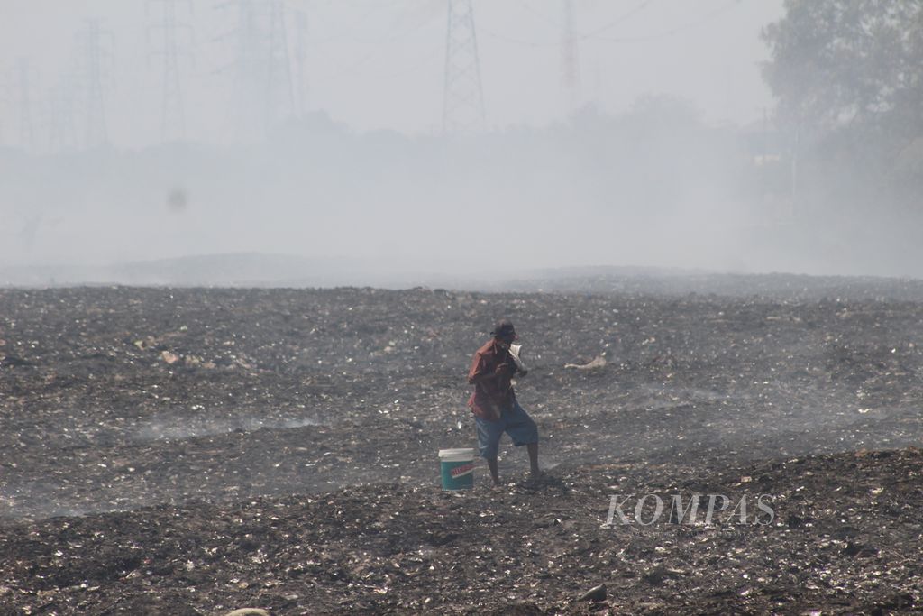 Seorang pemulung sedang mengambil beberapa barang di tempat pembuangan sampah ilegal yang terbakar di Desa Sumber Jaya, Kecamatan Tambun Utara, Kabupaten Bekasi, Selasa (26/9/2023).
