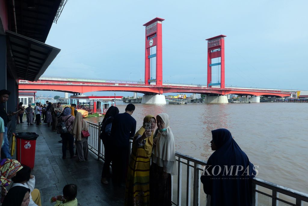 Sejumlah wisatawan berfoto dengan latar belakang Jembatan Ampera untuk mengisi masa libur Natal dan Tahun Baru di Palembang, Sumatera Selatan, Kamis (28/12/2023). Namun, saat malam pergantian tahun, jajaran Pemerintah Kota Palembang sepakat untuk membatasi kegiatan di tujuh pusat berkumpul pedagang ataupun masyarakat hingga pukul 22.00 pada Minggu (31/12/2023) dan melarang penyalaan petasan ataupun kembang api.