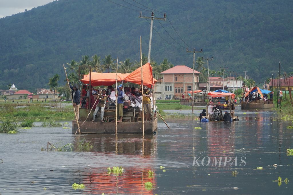 Warga menumpang perahu petambang pasir untuk melintasi jalan provinsi yang terendam banjir akibat meluapnya Danau Kerinci di Desa Semerap, Kecamatan Keliling Danau, Kabupaten Kerinci, Jambi, Selasa (16/1/2024). 