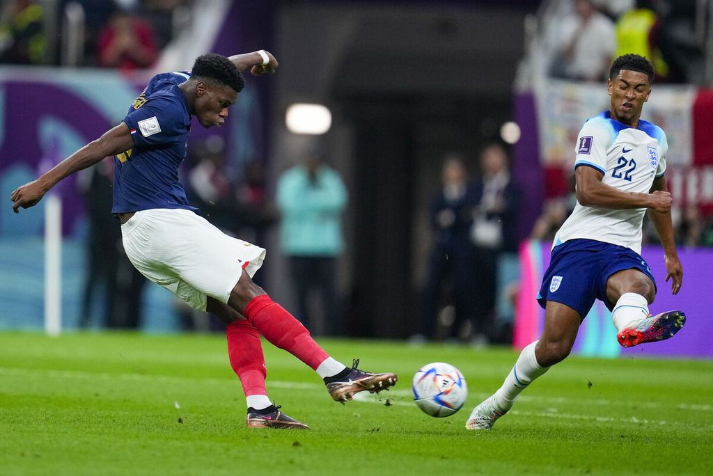 Pemain Perancis, Aurelien Tchouameni (kiri), menendang bola dan mencetak gol pembuka timnya dikawal pemain Inggris, Jude Bellingham, dalam pertandingan sepak bola perempat final Piala Dunia antara Inggris dan Perancis, di Stadion Al Bayt di Al Khor, Qatar, pada 10 Desember 2022. 