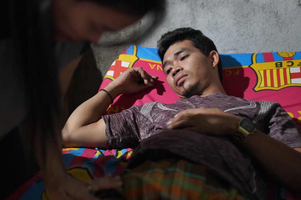 Muhammad Syafi’i (32) diobati Dinda, istrinya, di rumahnya di Desa Selorejo, Kabupaten Gunungkidul, DI Yogyakarta, Rabu (26/7/2023). Syafi’i saat ini menderita kerusakan saraf pada bagian tubuhnya imbas dari kecelakaan kerja yang dialami ketika menjadi anak buah kapal migran di kapal China pada pertengahan 2021 silam. Dalam kecelakaan kerja itu, Syafi’i mengalami luka bakar serius karena ketumpahan minyak mendidih.