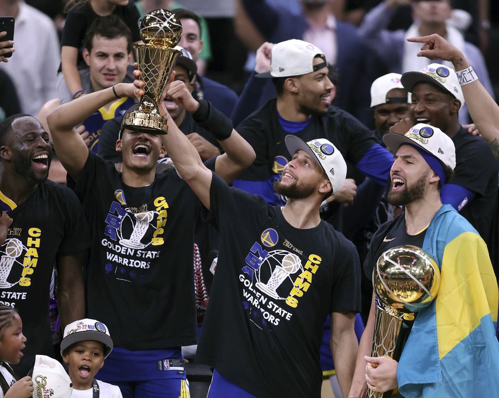 Stephen Curry (tengah) mengacungkan trofi MVP Final NBA disaksikan rekannya, Klay Thompson (kanan) yang memegang trofi juara NBA setelah membawa Golden State Warriors menjadi juara NBA untuk keempat kalinya dalam delapan musim terakhir, dengan mengalahkan Boston Celtics di TD Garden, Boston, 16 Juni 2022.