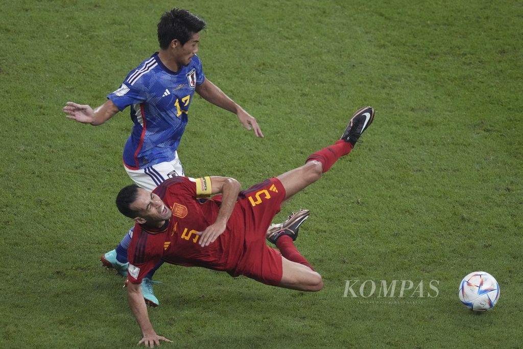 Pemain Spanyol Sergio Busquets terjatuh setelah diganjal pemain Jepang Hidemasa Morita dalam pertandingan di fase Grup E di Stadion Khalifa, Qatar, Jumat (02/12/2022) dini hari WIB. Jepang mengalahkan Spanyol 2-1. Jepang dan Spanyol lolos ke babak 16 besar Piala Dunia 2022. 