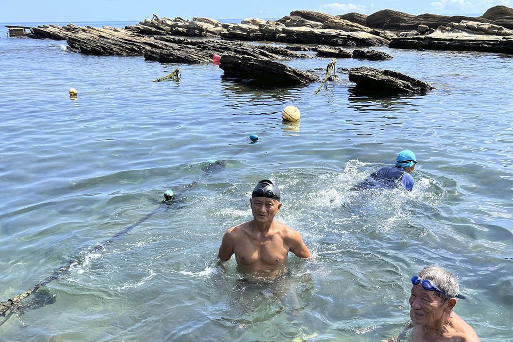 Dua orang warga Taiwan tengah berenang di Keelung, Taiwan, Kamis (4/8/2022) meski di laut lepas di belakang mereka militer China tengah melakukan latihan militer. (AP Photo/Johnson Lai)