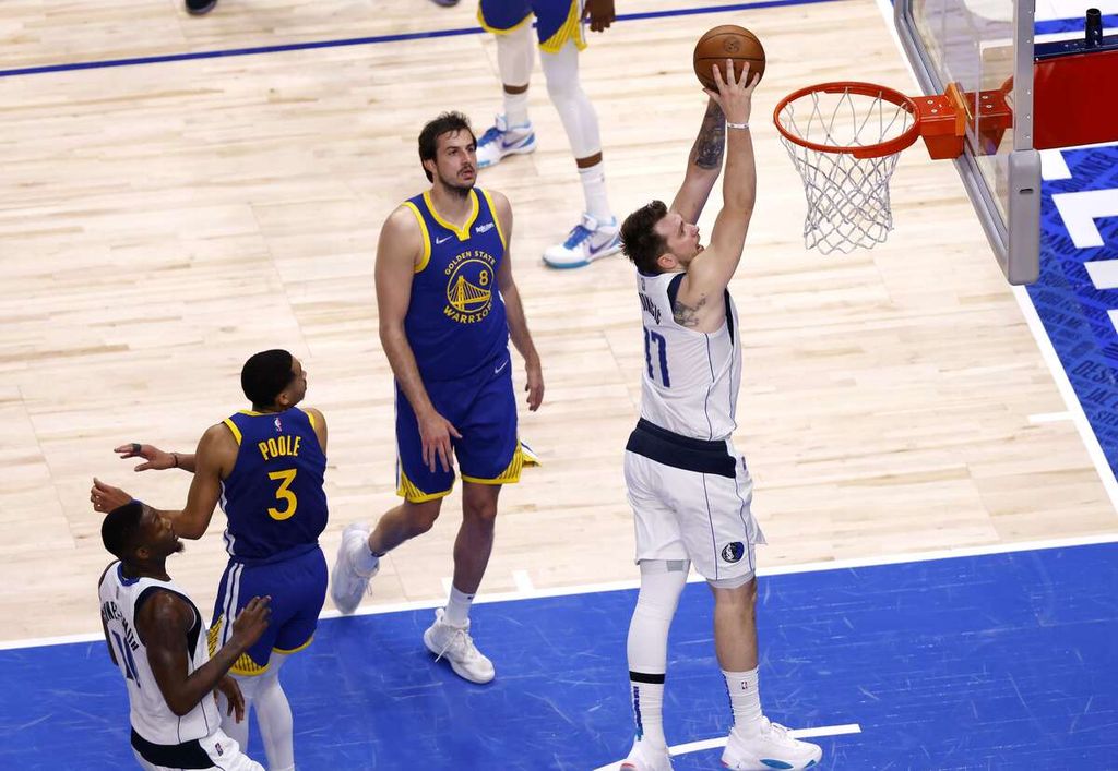 Pemain Dallas Mavericks, Luka Doncic, melakukan <i>dunk </i>melewati pemain Golden State Warriors, Jordan Poole, dalam pertandingan keempat final wilayah barat <i>playoff </i>NBA di American Airlines Arena, Dallas, Rabu (25/5/2022) siang WIB. Mavericks mengalahkan Warriors, 119-109. 