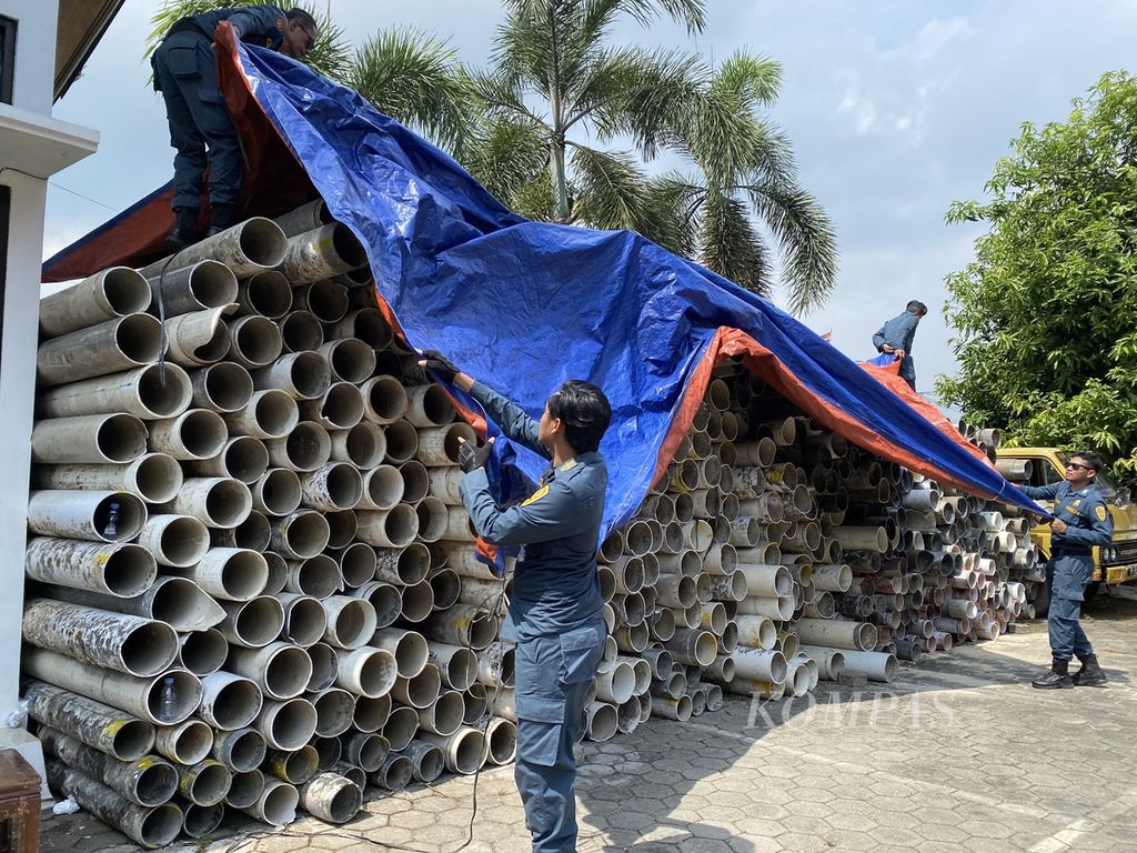 Petugas menutup ratusan pipa dengan terpal di halaman Kejaksaan Negeri Jepara, Jawa Tengah, Kamis (13/6/2024). 