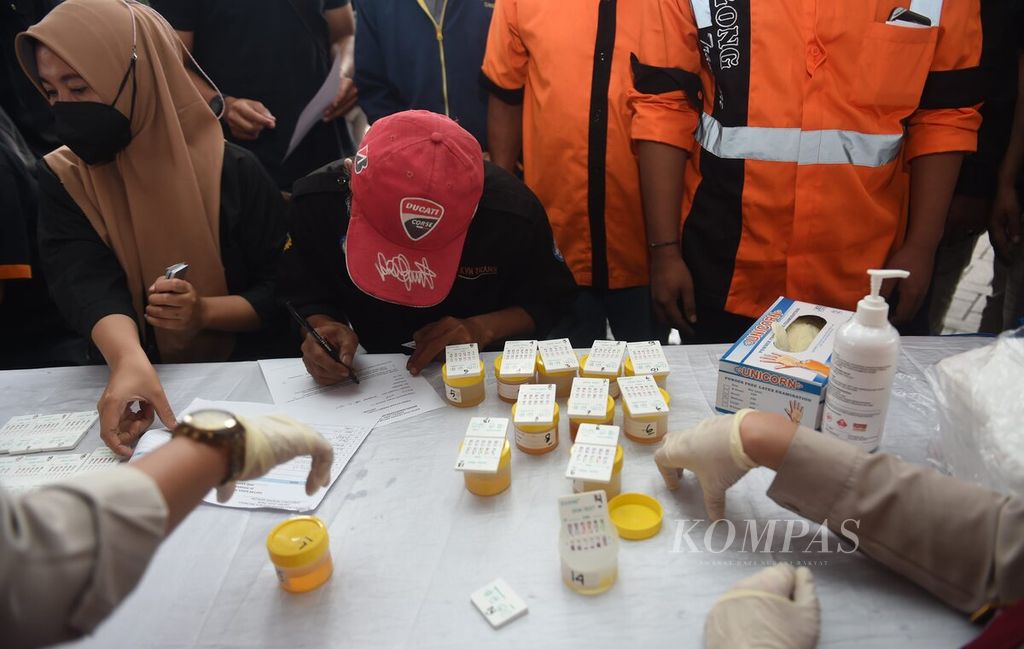 Sopir mengisi data diri, sementara petugas mengetes kandungan narkoba dalam urine saat giat tes urine bagi sopir bus yang diselenggarakan oleh Direktorat Reserse Narkoba Polda Jawa Timur di Terminal Purabaya, Kabupaten Sidoarjo, Jawa Timur, Kamis (22/12/2022).
