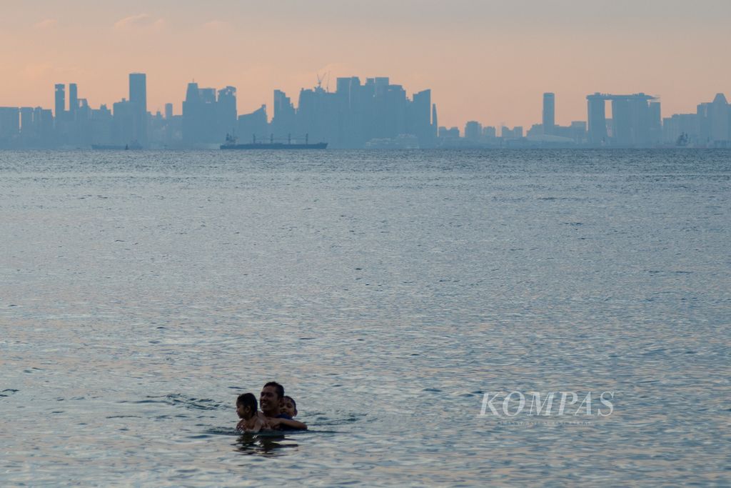 Warga berwisata di Pantai Tanjung Pinggir, Batam, Kepulauan Riau, Minggu (28/5/2023). Di lokasi itu, gedung-gedung pencakar langit Singapura tampak dari kejauhan.