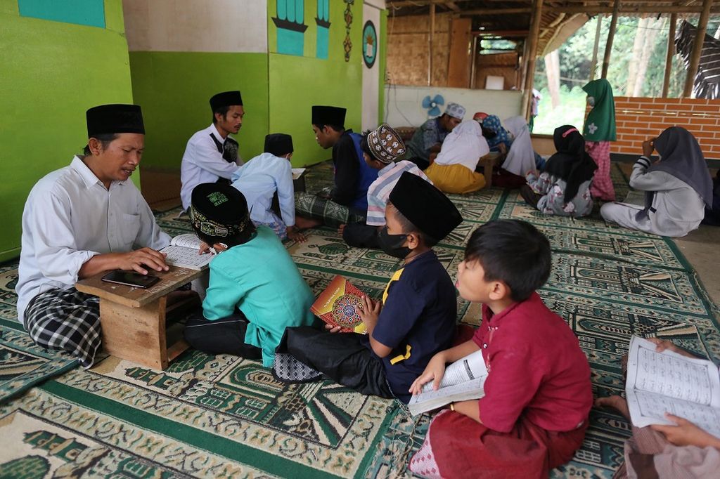 Taslim, seorang sopir truk pengangkut pasir (kiri), dibantu dengan murid yang sudah senior, mengajari anak-anak di kawasan Desa Cisauk, Kabupaten Tangerang, Banten, belajar mengaji, Sabtu (16/4/2022). Taslim tergerak untuk menjadi pengajar karena melihat banyak anak di kawasan tempatnya bekerja tidak bisa belajar membaca tulisan Arab.