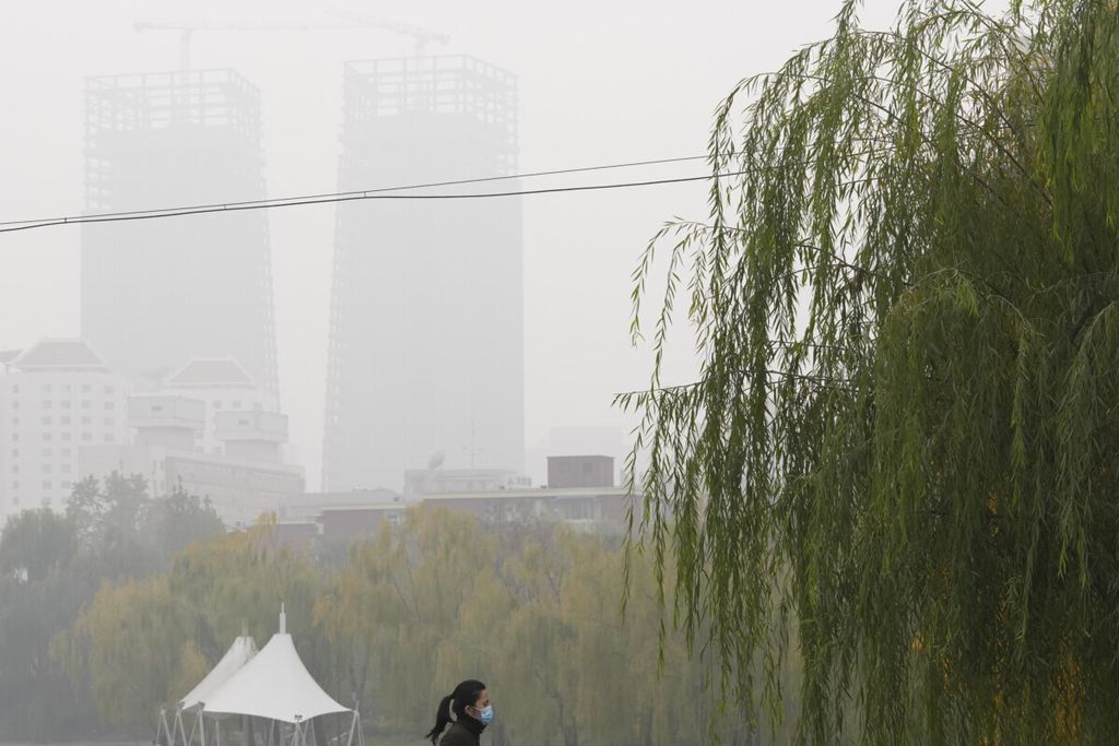 Perempuan mengenakan masker saat berjalan kaki dalam kondisi udara yang berpolusi di Beijing, China, awal November 2021.