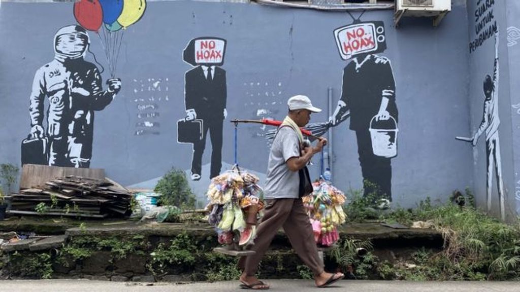 Warga melintasi mural yang dibuat untuk melawan penyebaran informasi palsu di masyarakat atau hoaks di Jalan KH Hasyim Ashari, Tangerang, Banten, Senin (22/2/2021).
