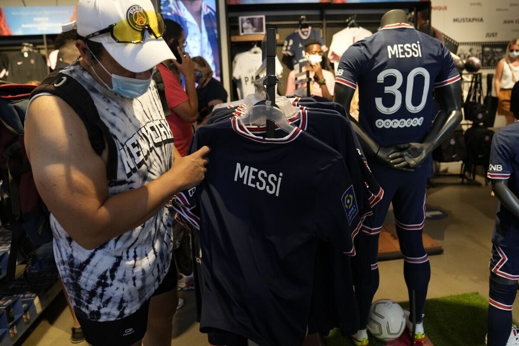 Seorang suporter PSG melihat jersei Lionel Messi di outlet resmi PSG di Paris, Perancis (11/8/2021). Kepindahan Messi ke PSG membuat jersei dan souvenir Messi banyak dibeli suporter PSG.