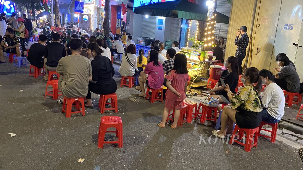 Para remaja hingga pekerja muda, baik pria maupun wanita, duduk menggunakan kursi pendek di pinggiran jalan di kawasan Old Quarter, Hanoi, Vietnam, Sabtu (14/5/2022). Mereka biasanya menikmati kuaci bunga matahari ditemani aneka minuman dingin dan membicarakan banyak hal bersama rekan-rekannya.