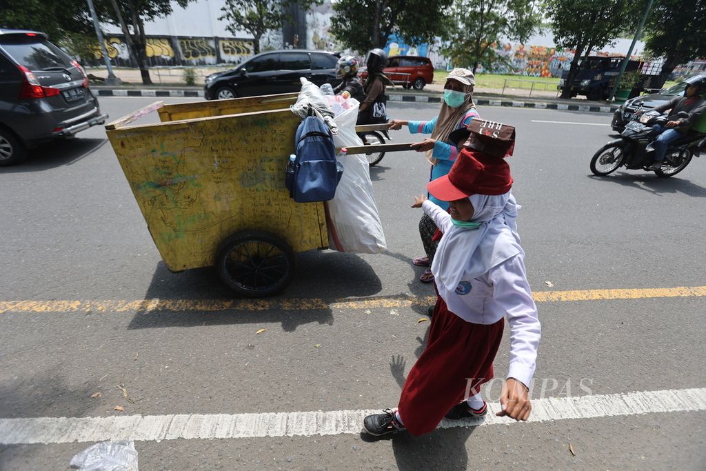 Sri Subekti (46) melintas di kawasan Kotabaru, Yogyakarta, saat menjemput anak-anaknya, Nisabela Putri (10) dan Idham Al Ghozali (9), pulang dari sekolah, Senin (28/3/2022). Kegiatan mengantar dan menjemput kedua anaknya dari sekolah itu dilakukan sambil mencari sampah yang dapat dijual kembali.