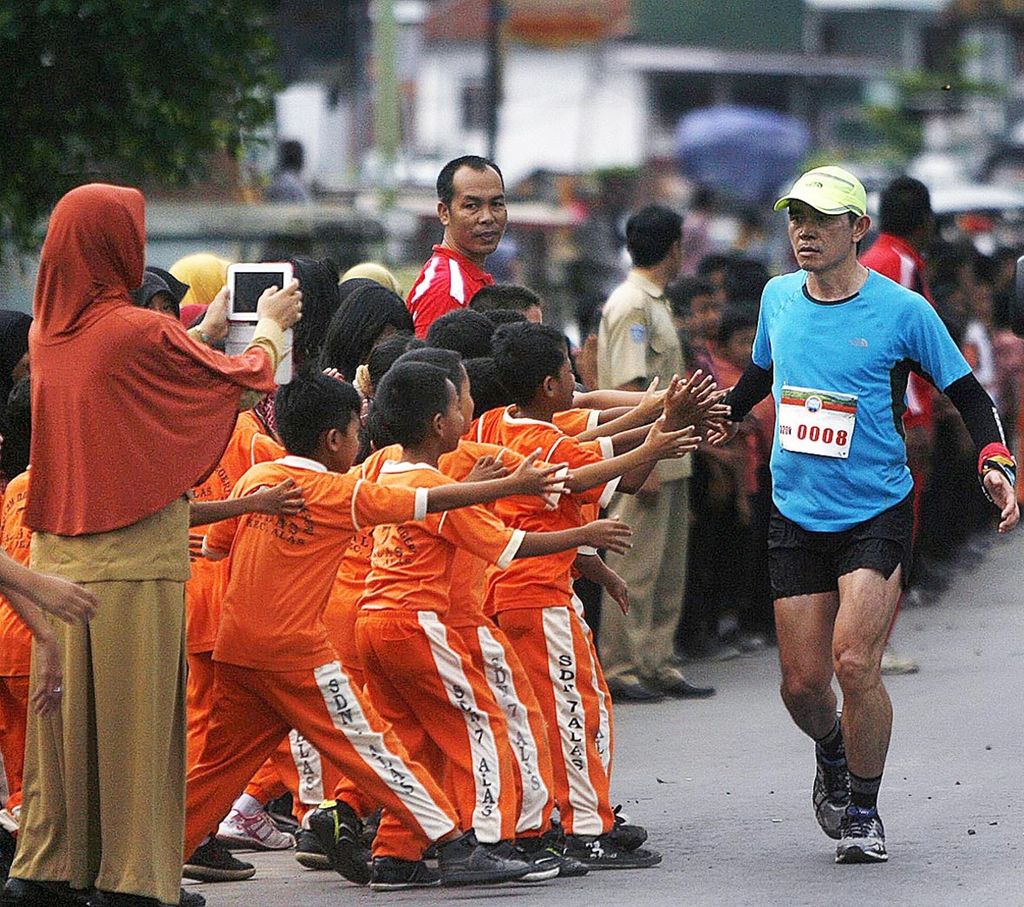 Tambora Challenge 2015 - Hendra Wijaya, peserta lomba lari Trans Sumbawa dalam rangkaian Tambora Challange 2015 lintasi disambut siswa SD Negeri Alas 7 di Kecamatan Alas, Sumbawa, NTB, Rabu (8/4). Lomba lari yang diikuti 8 peserta dengan 25 pelari pendamping ini dilepas dari Poto Tano dan finis di Doro Ncanga yang berjarak sekitar 320 kilometer. Kompas/Rony Ariyanto Nugroho (RON) 08-04-2015