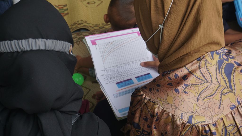 Seorang ibu melihat grafik tumbuh kembang anak yang ada di buku KIA (kesehatan ibu dan anak) saat membawa anaknya dalam pelayanan di Posyandu Mawar Merah, Dusun Klangon, Sedayu, Bantul. DIY, Jumat (10/2/2023).