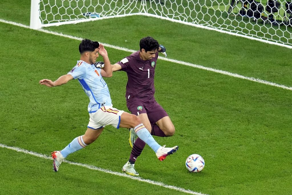Kiper Maroko Yassine Bounou berusaha keras mengamankan bola dari pemain Spanyol Marco Asensio dalam pertandingan babak 16 besar Piala Dunia Qatar di Stadion Education City di Al Rayyan, Qatar, Selasa (6/12/2022). Maroko yang kalah dalam penguasaan bola justru beberapa kali mendapatkan peluang menciptakan gol melalui serangan balik.